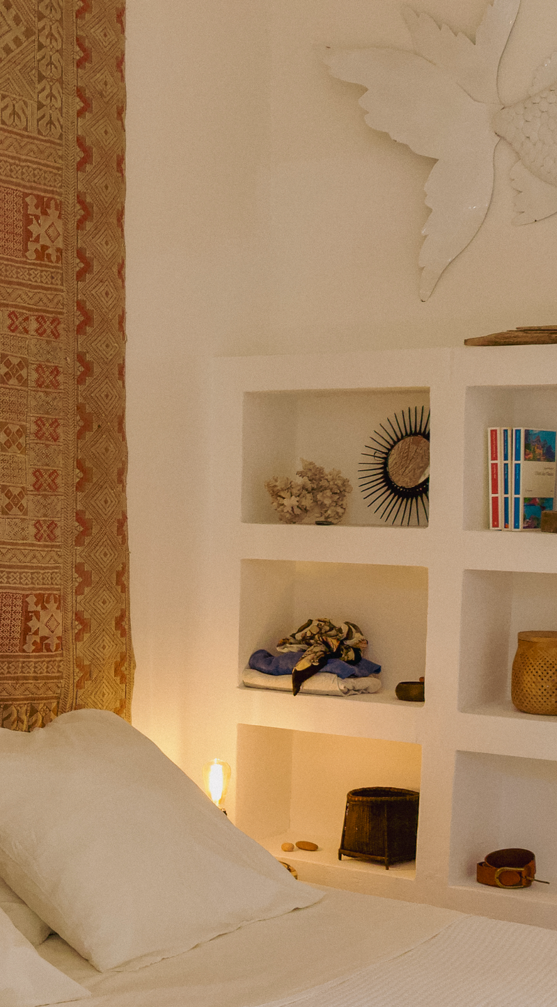 Bedroom with a shelf displaying decorative items and a patterned curtain.