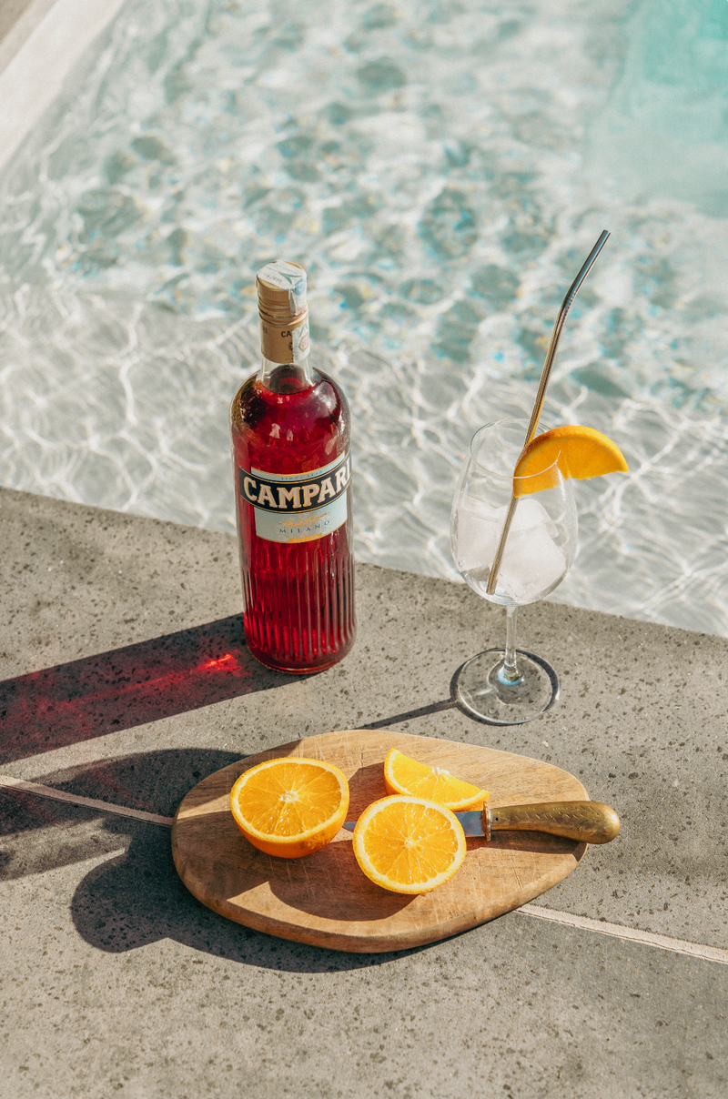 Campari bottle with a glass and oranges by a pool