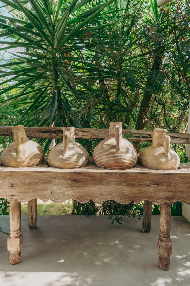 Four ceramic jugs on a wooden table with a natural outdoor background