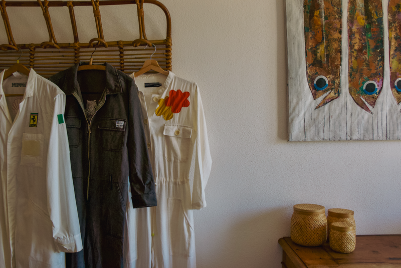 Clothing hanging on a rack with a wall painting and jars in the background