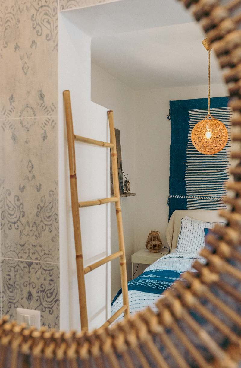 Bathroom with decorative tiles, a wooden ladder, and a bedroom with a bed and lamp.