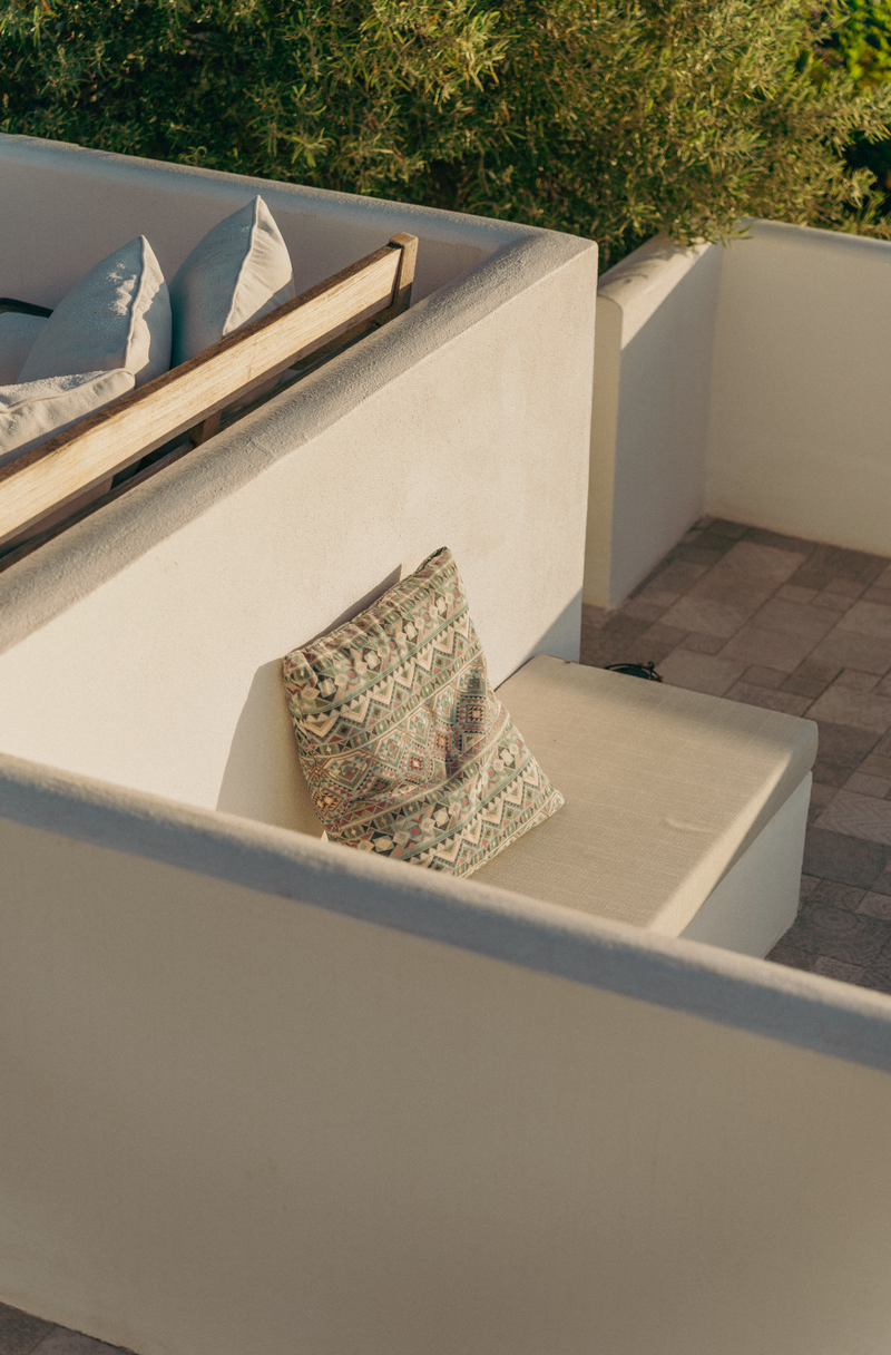 Outdoor seating area with white cushions and a wooden bench on a patio.