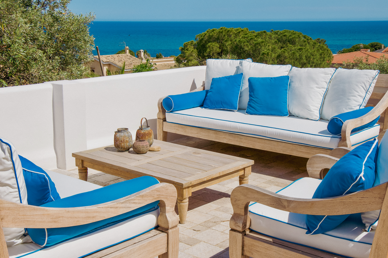 Outdoor patio set with wooden furniture and blue cushions overlooking the ocean.