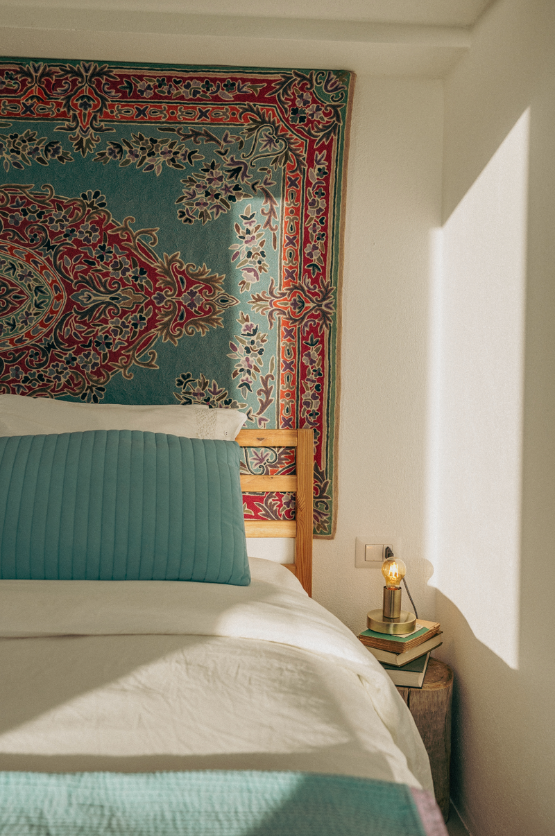 Bedroom with a colorful tapestry on the wall, bed with teal bedding, and lamp on a nightstand.