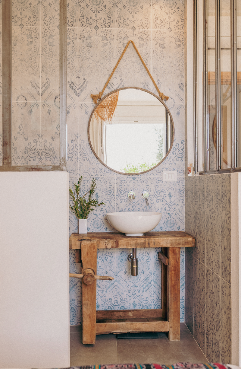 Bathroom with wooden vanity, round mirror, and decorative tiles.